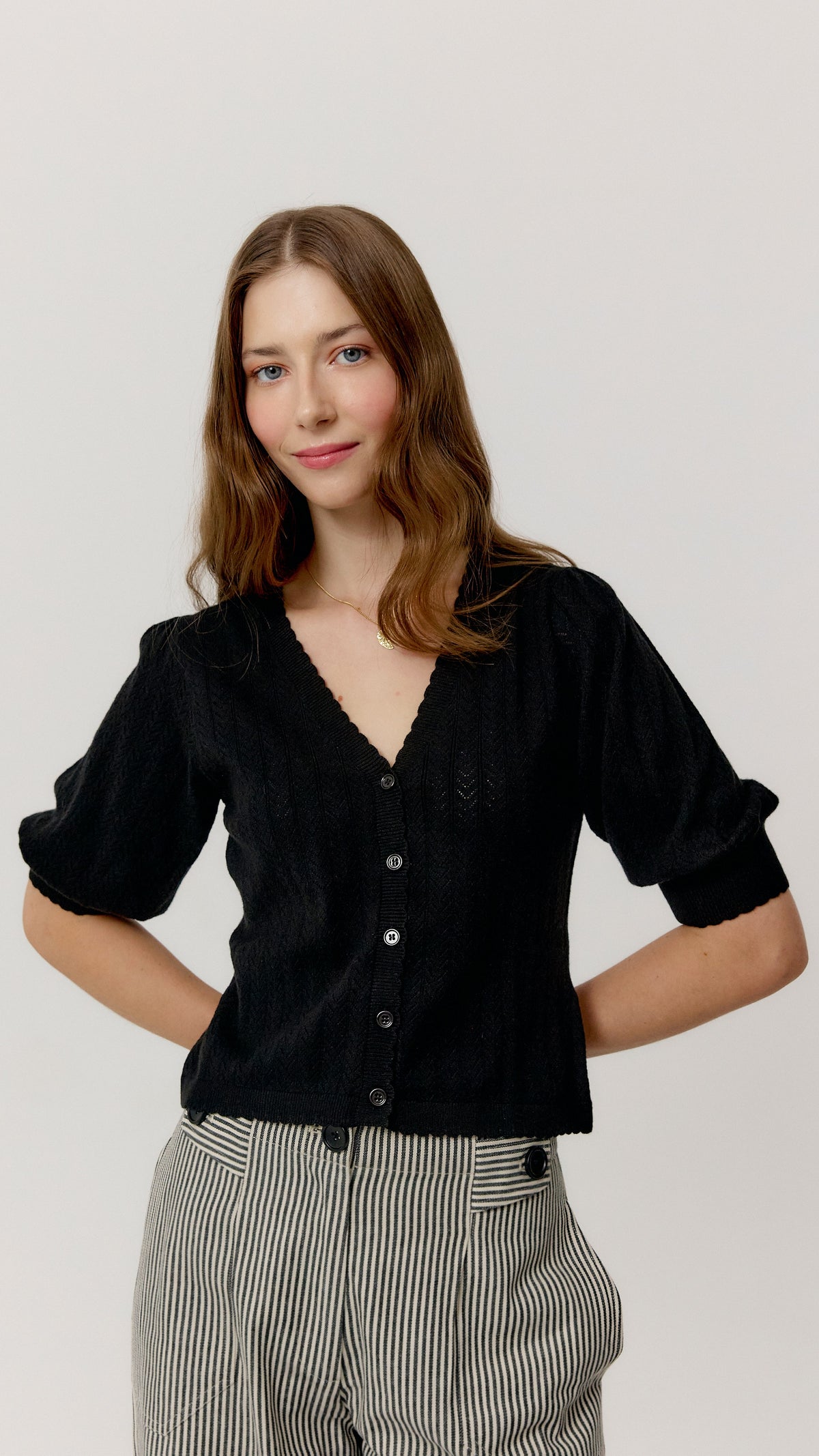 Top Ada negro con manga corta abullonada y bajo ondulado, vista frontal.