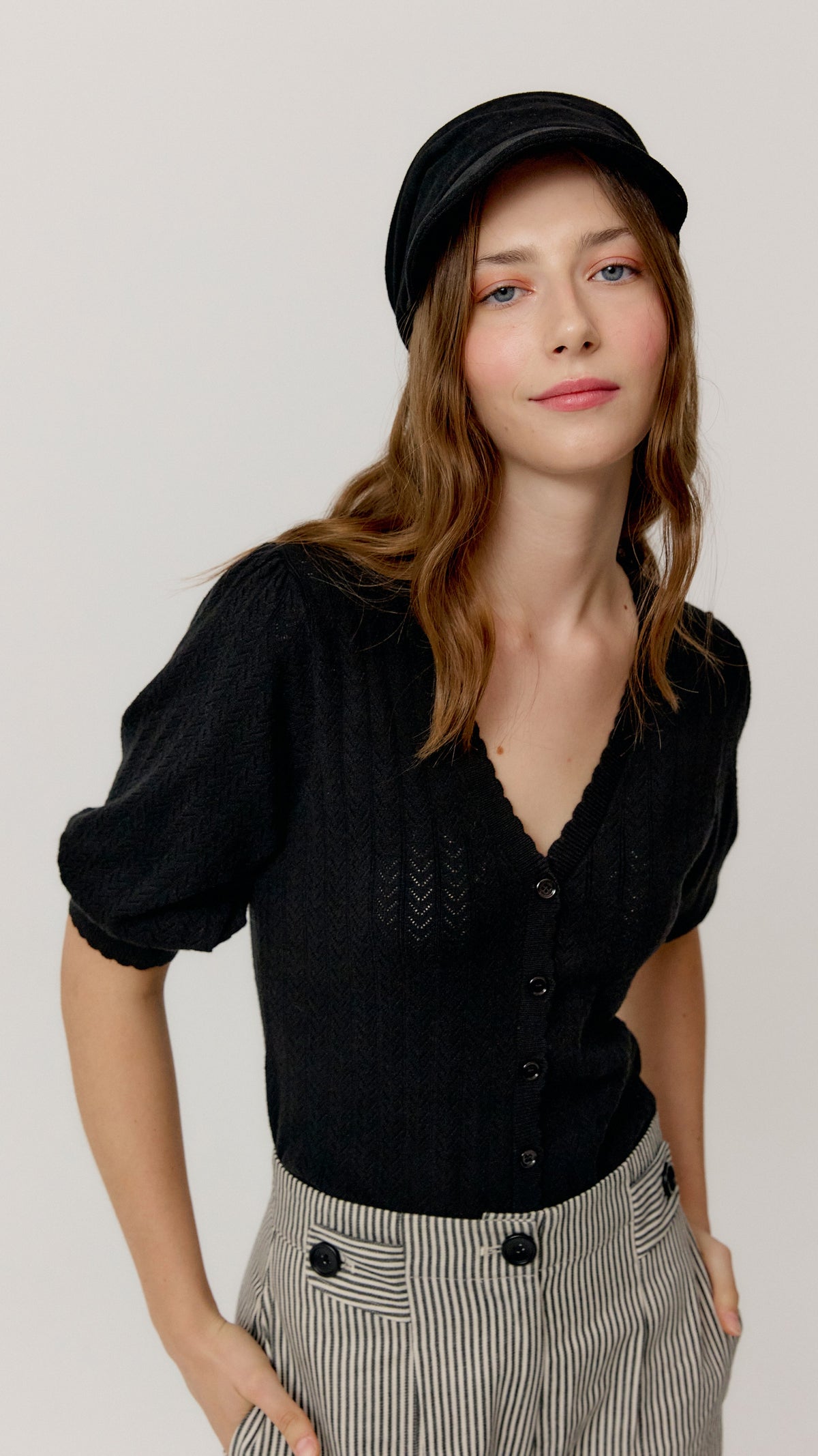 Top Ada negro con escote en V, combinado con gorra negra y pantalón de rayas.